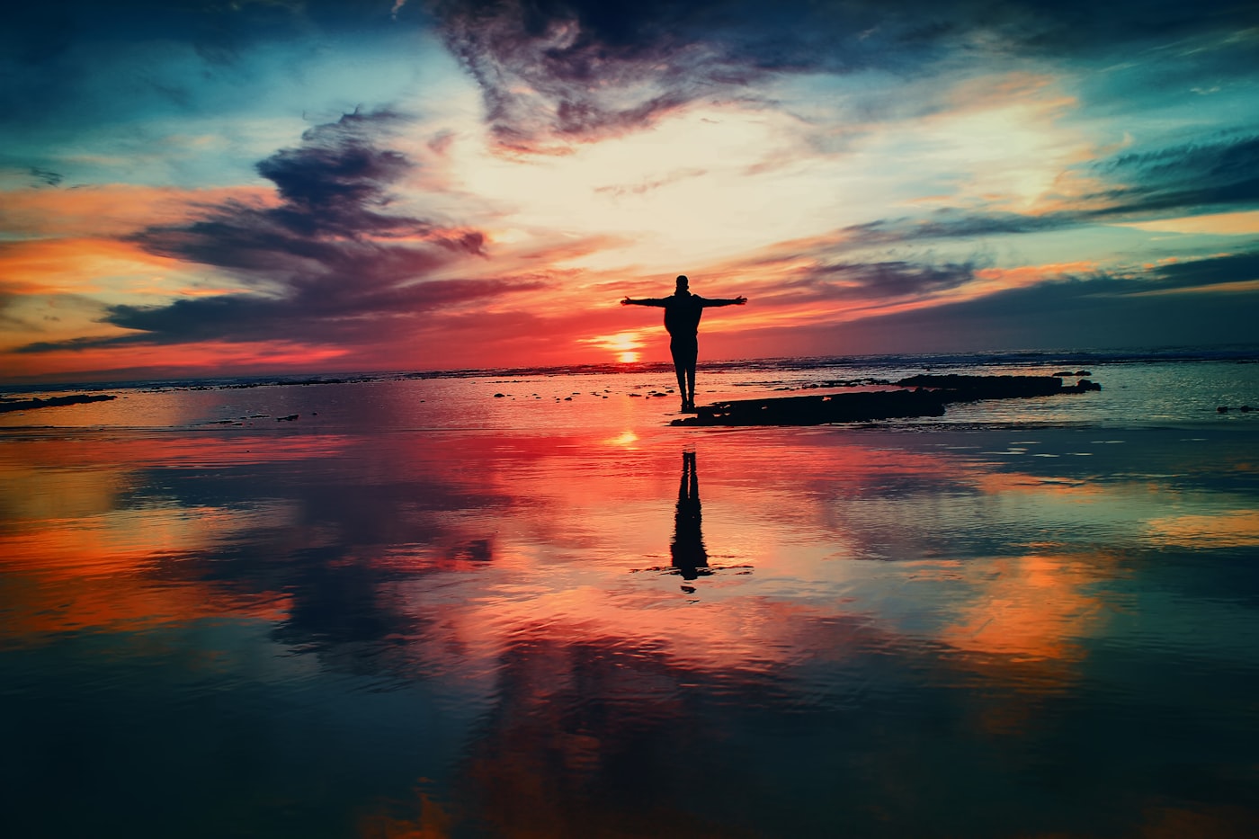 A person standing by the sea at sunset, arms outstretched